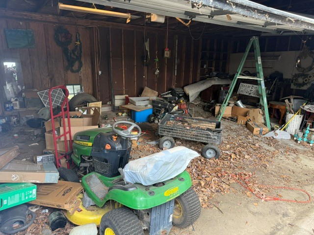 Cluttered garage with mower, boxes, and mixed household items before junk removal